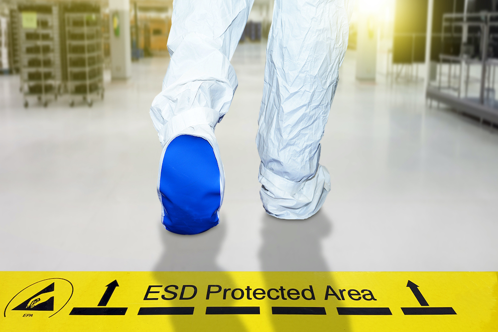 Man walking on a floor of the scientific laboratory covered industrial linoleum pastes a yellow tape with a standard warning text: "ESD Protected Area"